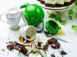 A messy table with spilled mugs and cake crumbs
