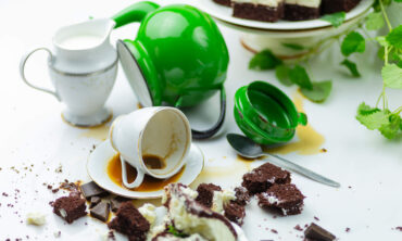 A messy table with spilled mugs and cake crumbs