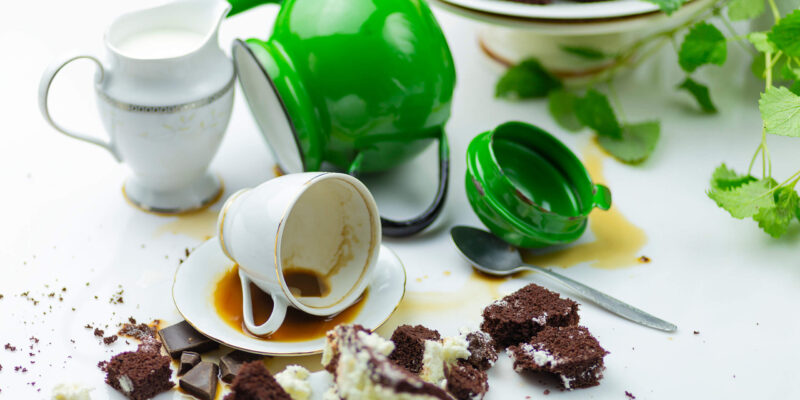 A messy table with spilled mugs and cake crumbs